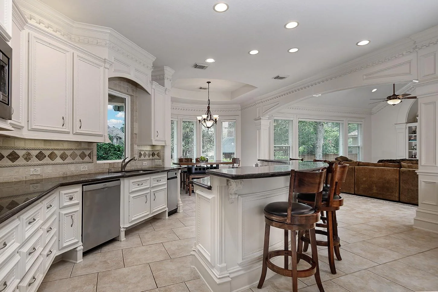 Chef's kitchen with white custom cabinetry, dark granite island, breakfast bar stools, and open view to family room