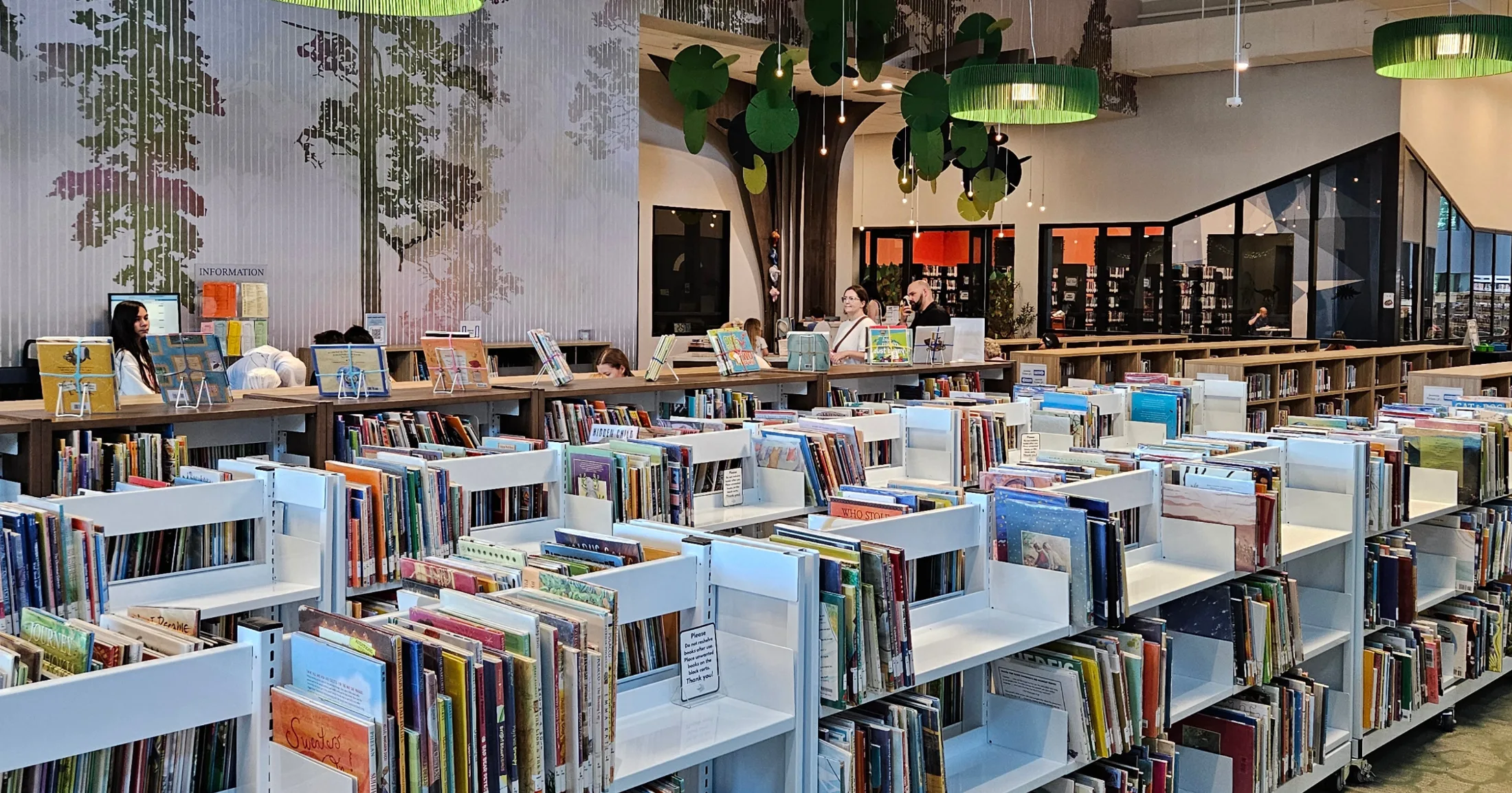 Children's section of the Kevin Brady Library with low shelves, world map mural, and sculptural tree feature