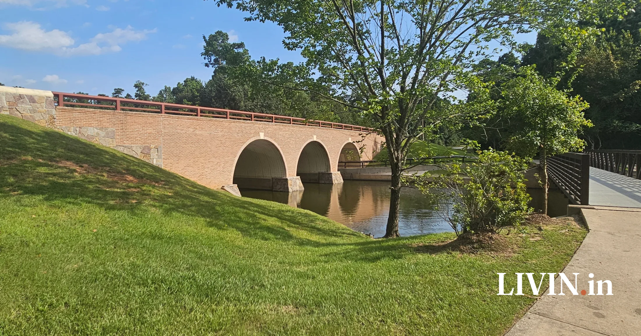 Brick arch bridge spanning a calm waterway alongside a walking path in The Woodlands, Texas