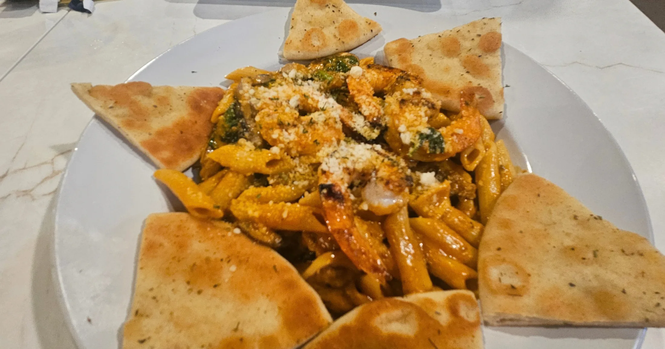 Vodka Shrimp Penne in creamy tomato sauce topped with cheese, surrounded by warm pita wedges