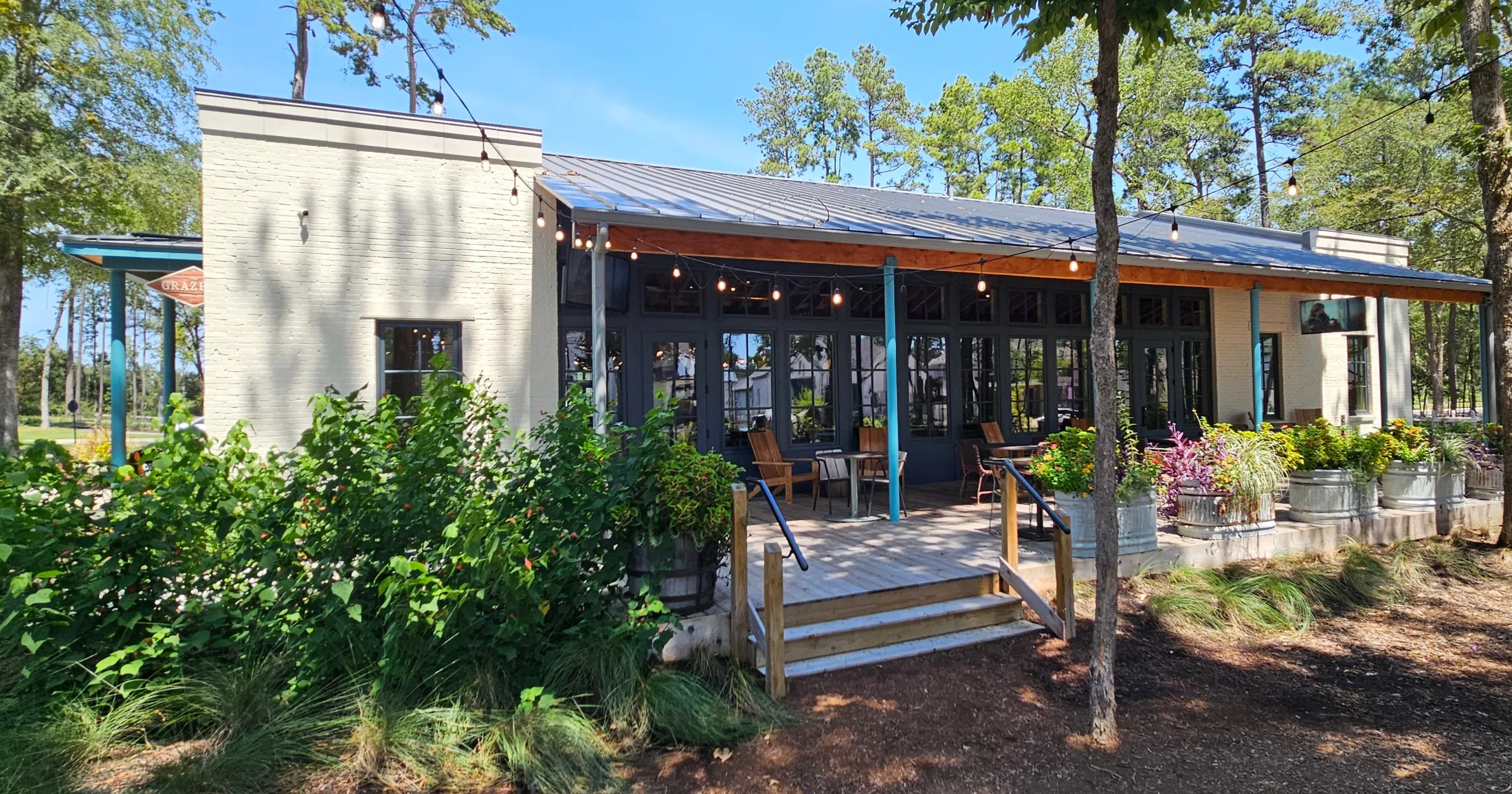 Covered outdoor patio with string lights, wood deck, and open glass doors surrounded by gardens