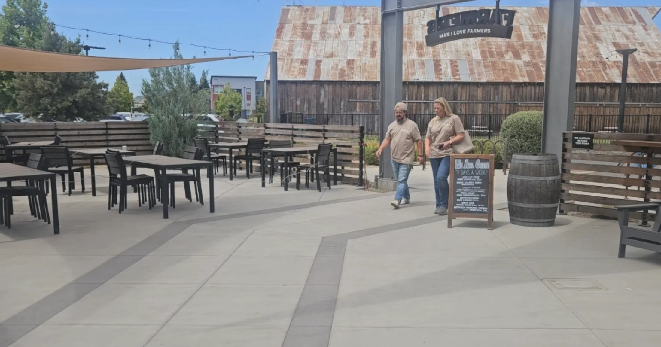 The outdoor patio at Farmers Brewing Co. in Chico, with two founders walking past the rustic barn facade and 'Man I Love Farmers' signage