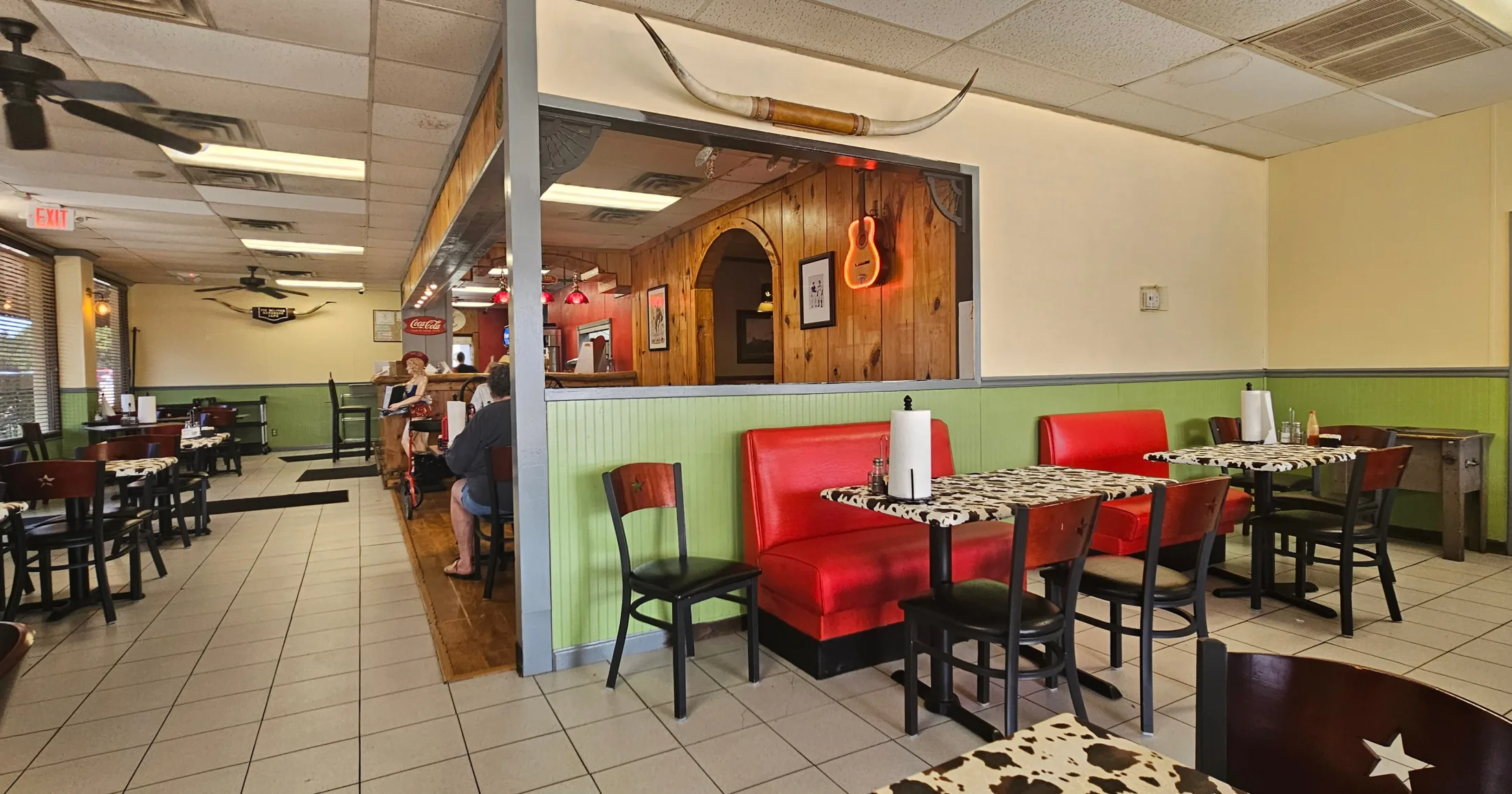 Interior dining room at Pit Master Bar-B-Que with red booths, cow-print tables, and Western decor