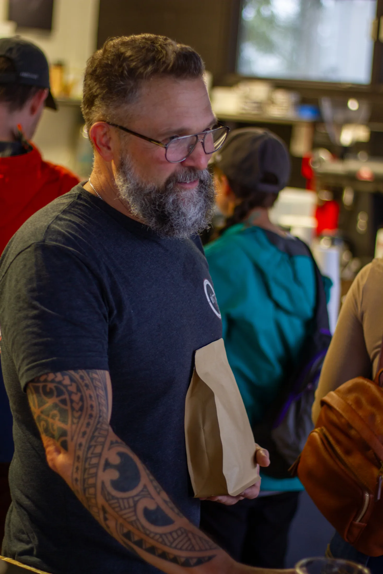 David Dunlap in a 1677 Coffee Co. shirt handing a kraft paper bag of coffee to a customer inside the busy cafΓ©