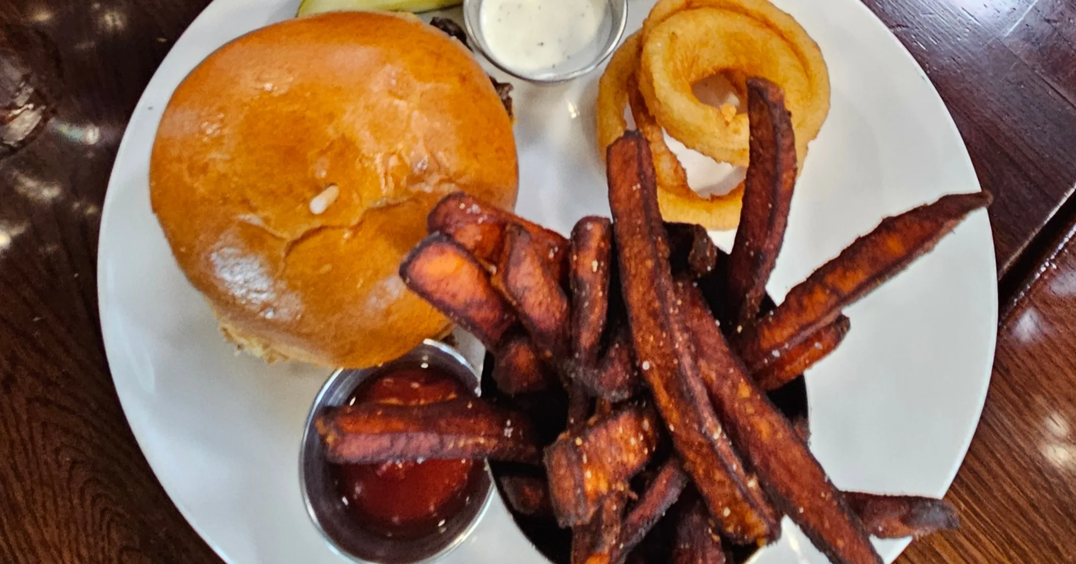 A brioche bun sandwich with sweet potato fries and onion rings at Farmers Brewing Co.