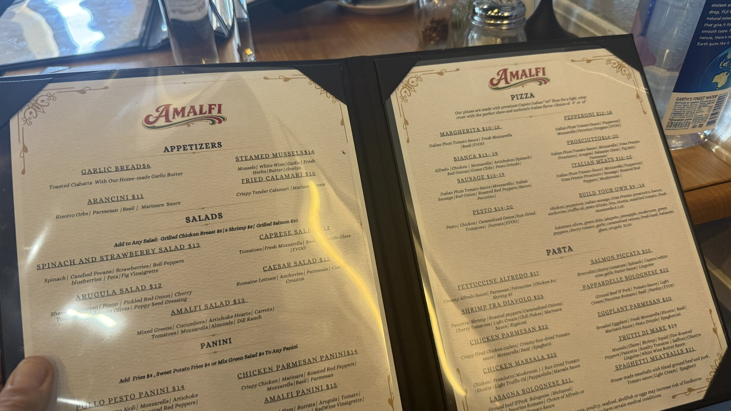 Two pages of the Amalfi menu with the name Amalfi in red script, held over a wood table