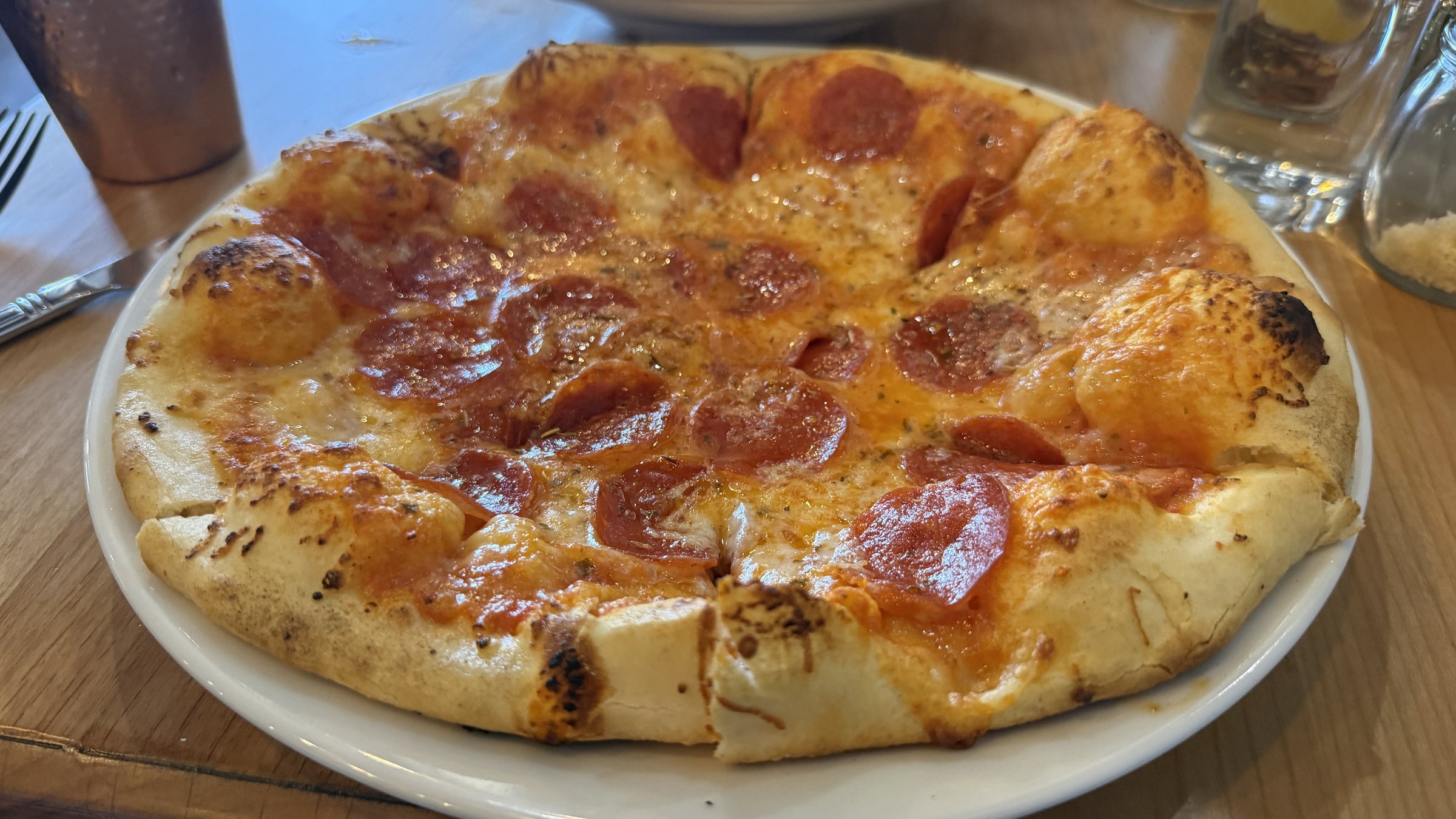 A pepperoni pizza with a puffed, browned crust on a white plate at Amalfi