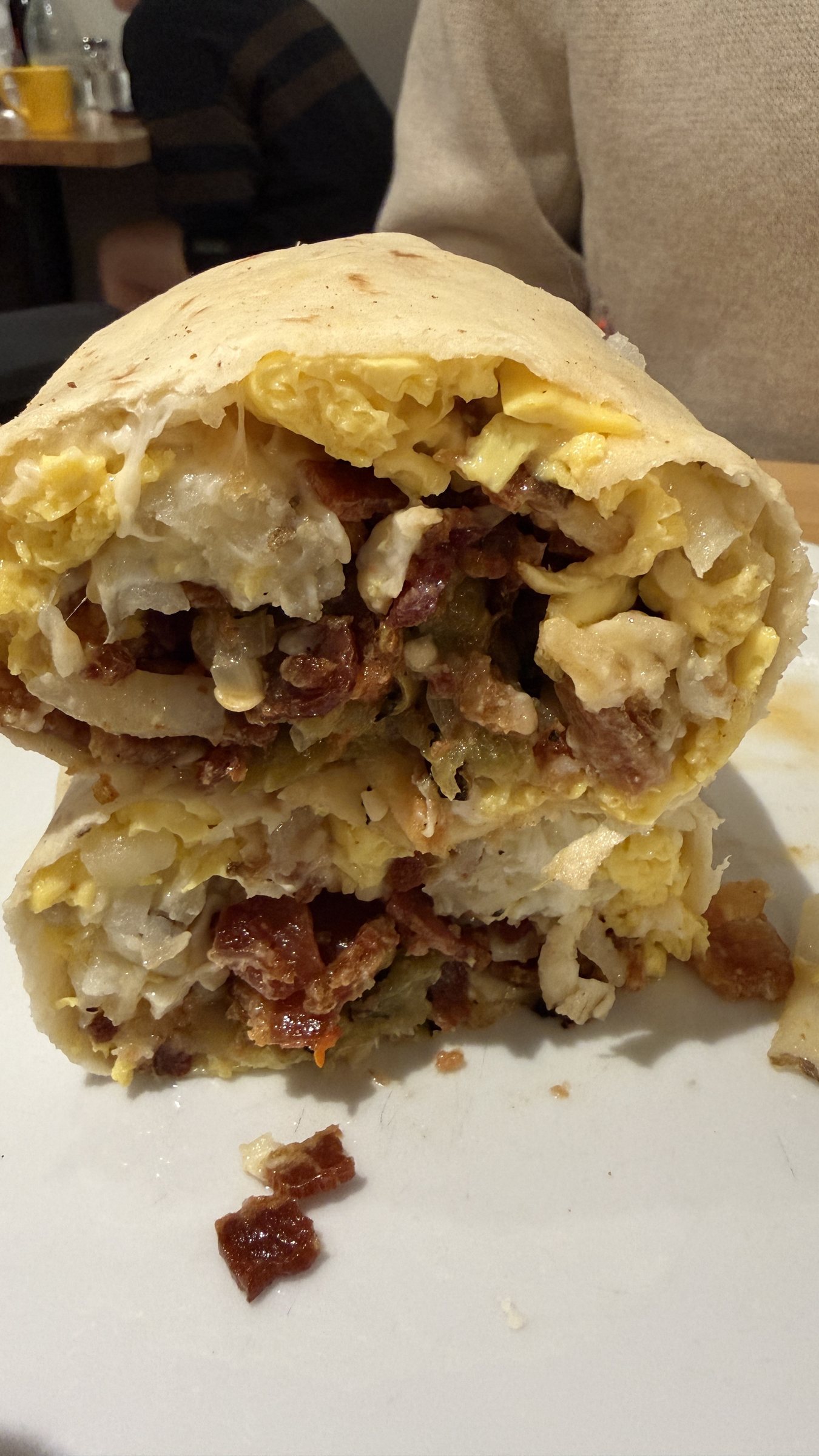 A breakfast burrito cut in half showing scrambled eggs, bacon, potatoes, green chile and melted cheese