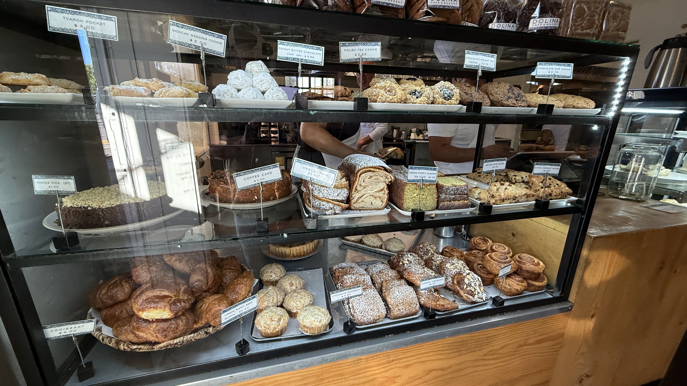 A glass pastry case with cookies, scones, croissants and coffee cake, each with a printed price label