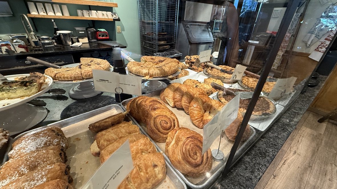 A Cafe Fina pastry case with croissants, cinnamon rolls and other pastries on trays