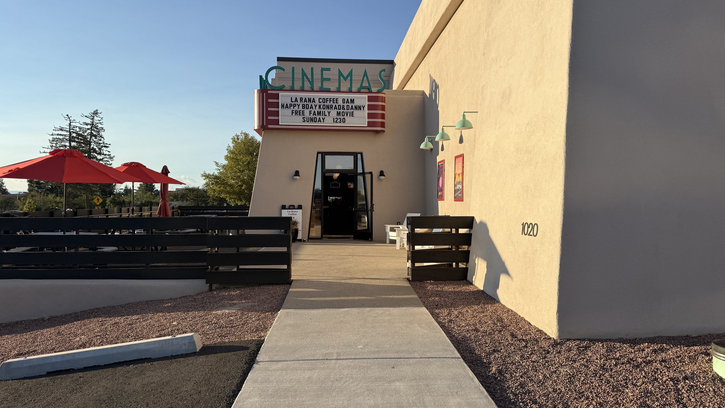 The Sky Cinemas Midtown exterior, with a CINEMAS sign, a marquee reading La Rana Coffee 8AM and red umbrellas over a fenced patio