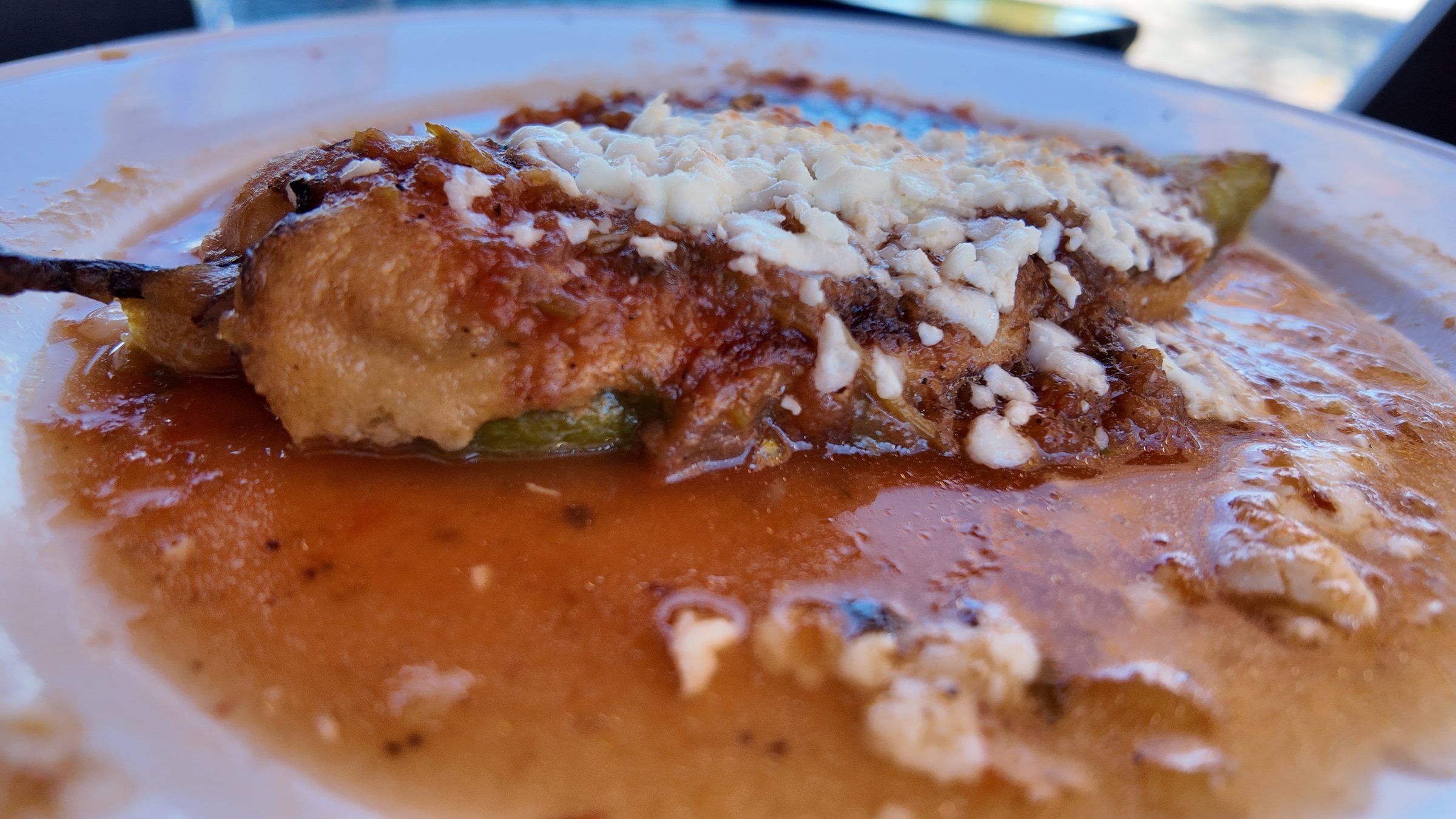 A chile relleno in tomato salsa with crumbled cheese