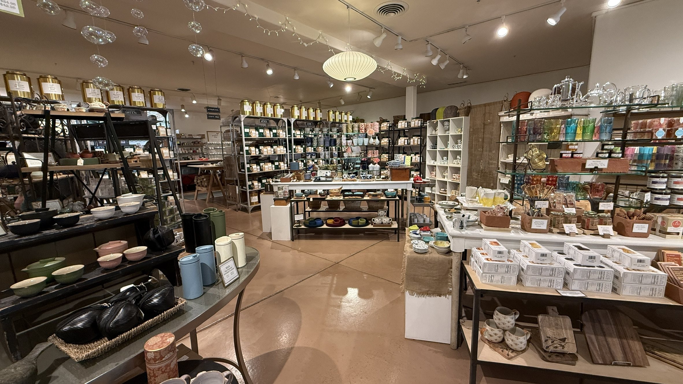 Shelves of gold tea tins, boxed teas, teapots, cups and colored glassware inside ArtfulTea