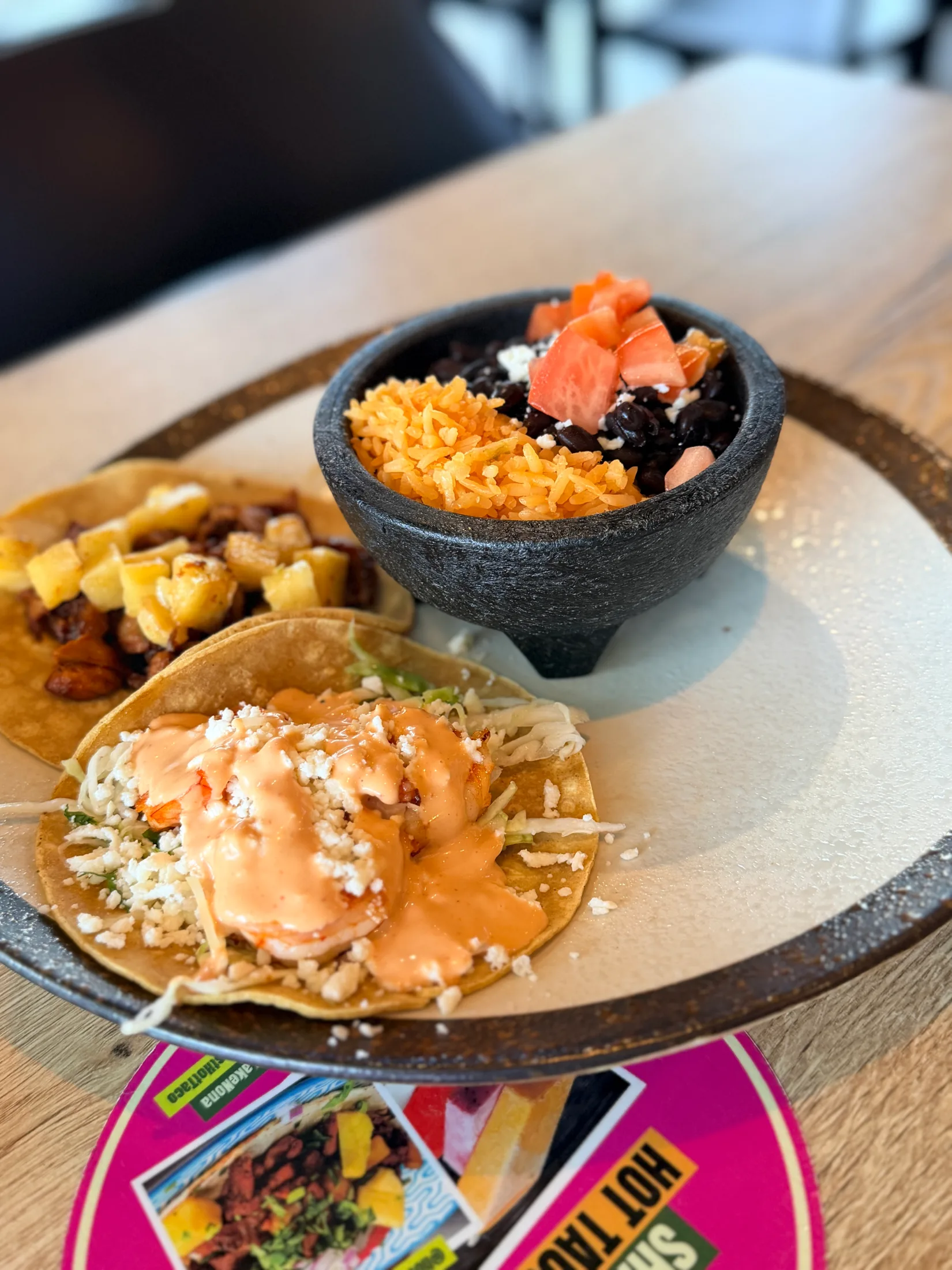 Tacos on corn tortillas with shrimp and chipotle sauce next to a stone bowl of rice and black beans at Hot Taco Street Taqueria