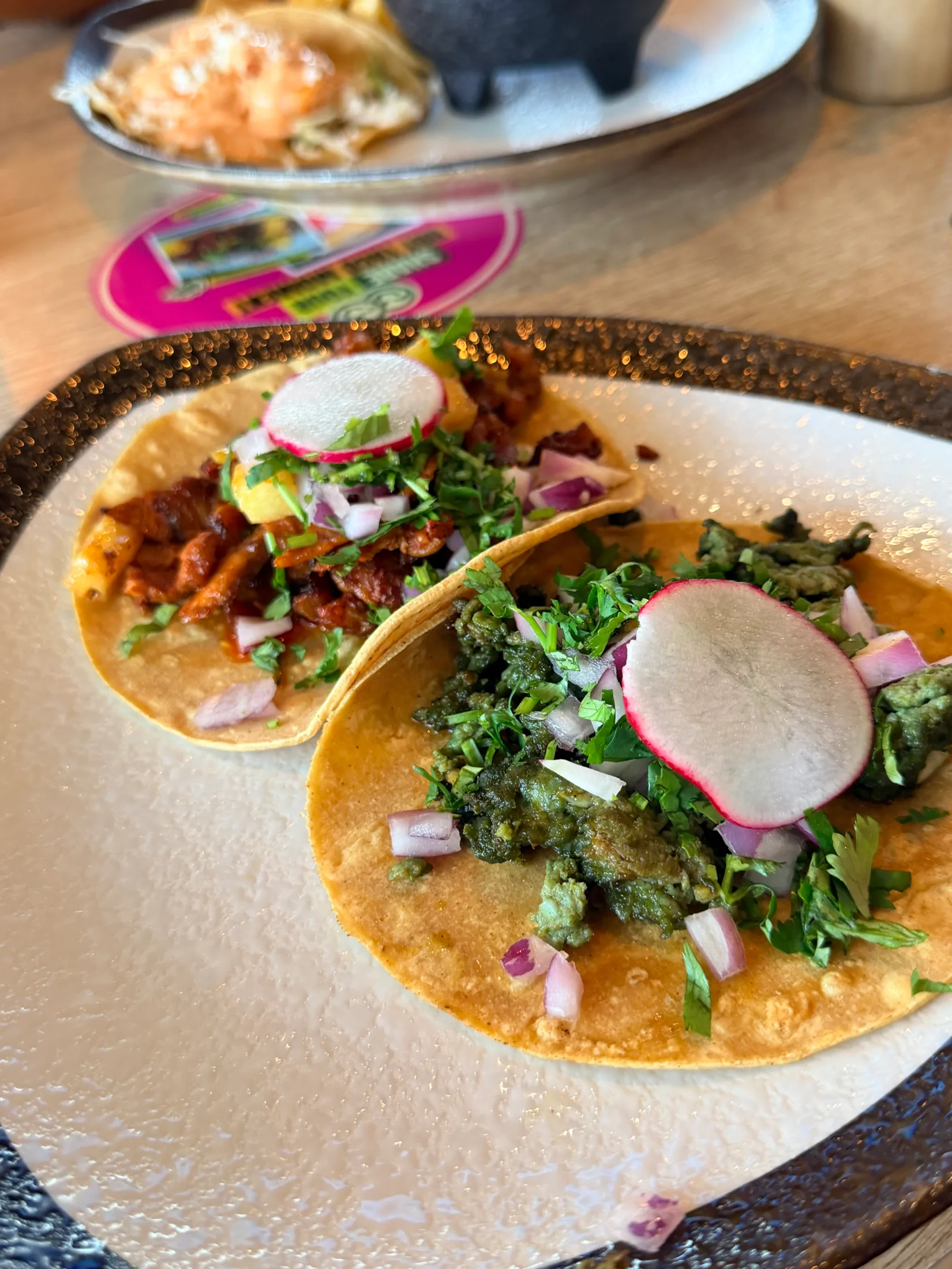 Two handcrafted tacos on corn tortillas with cilantro, red onion, and sliced radish at Hot Taco Street Taqueria