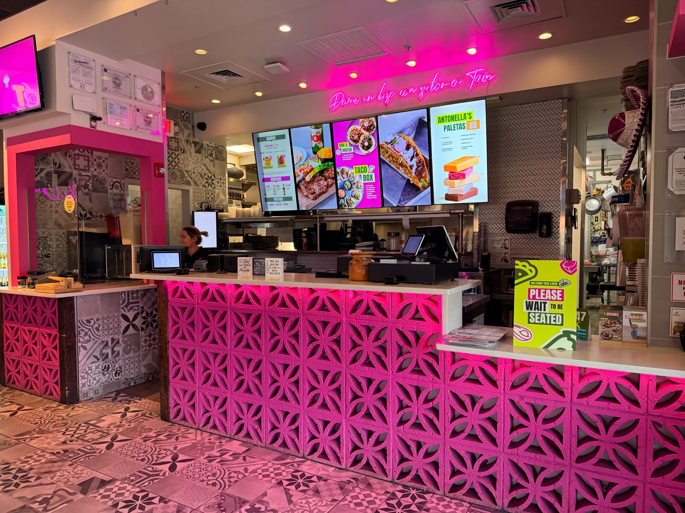 Flower-covered hallway with purple neon lighting and Carta y no llores neon sign at Hot Taco Street Taqueria