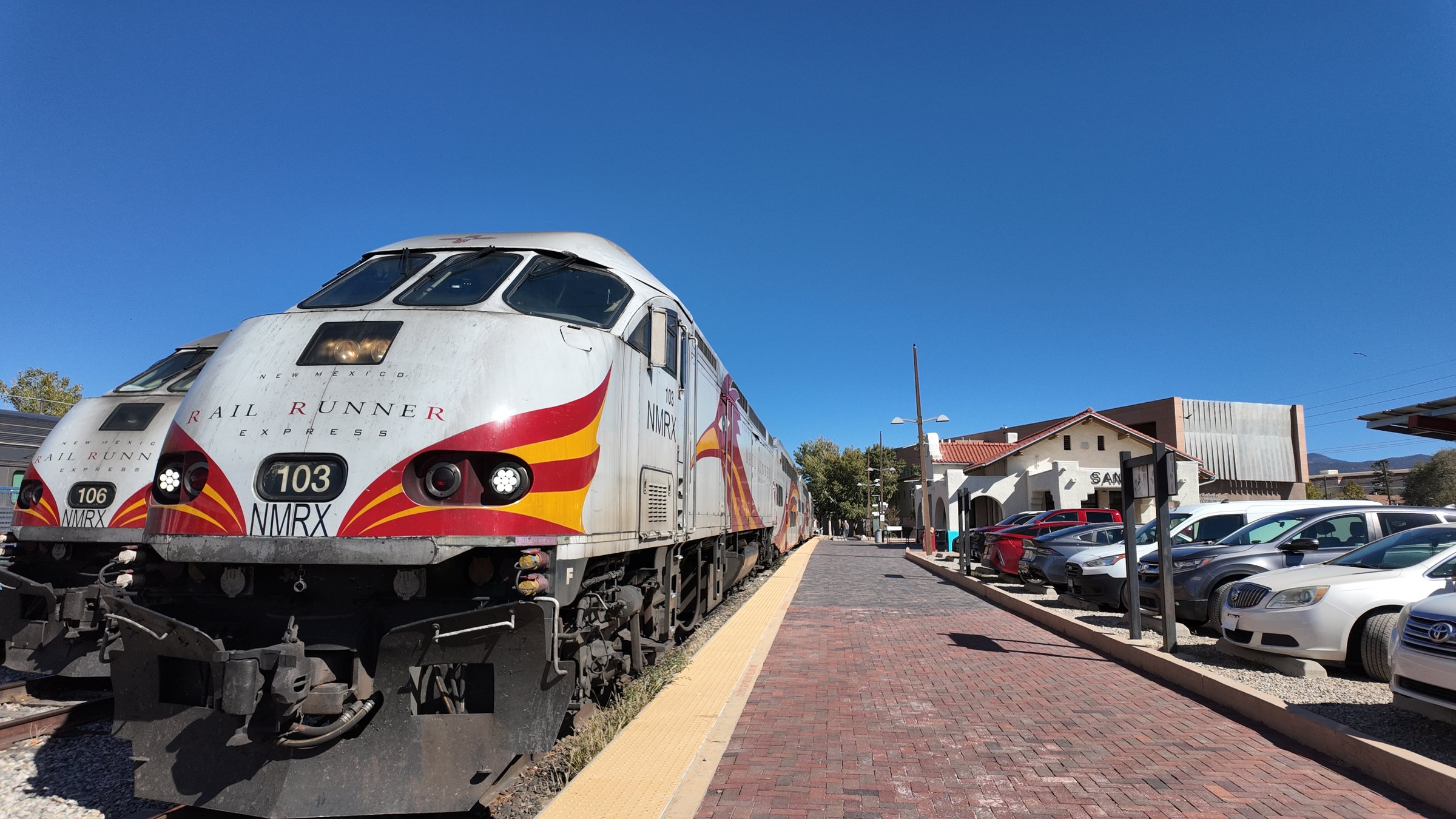 Rail Runner locomotive 103 nose on the brick platform, with the Santa Fe depot behind