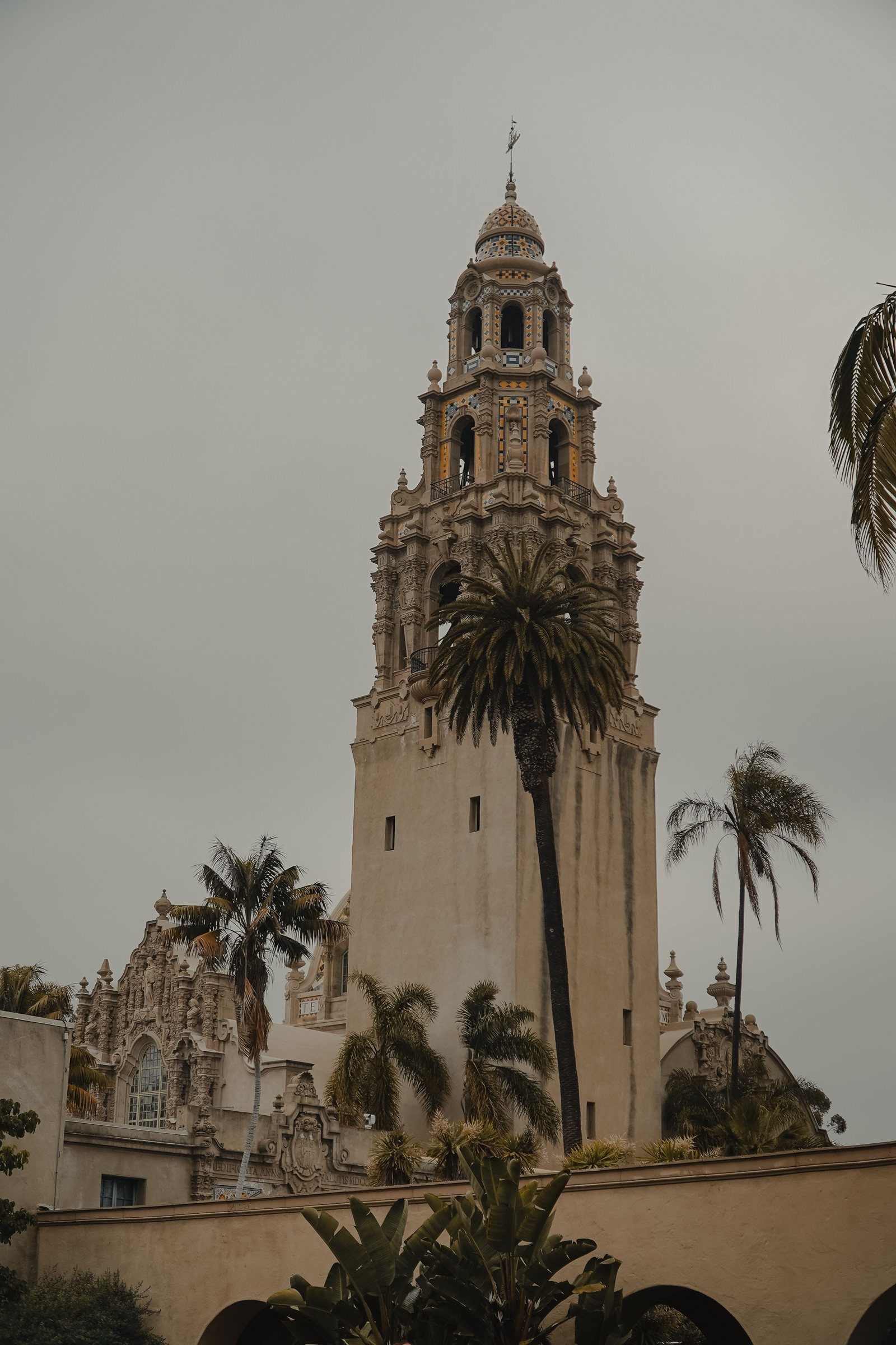 The California Tower in Balboa Park with palm trees on a cloudy day