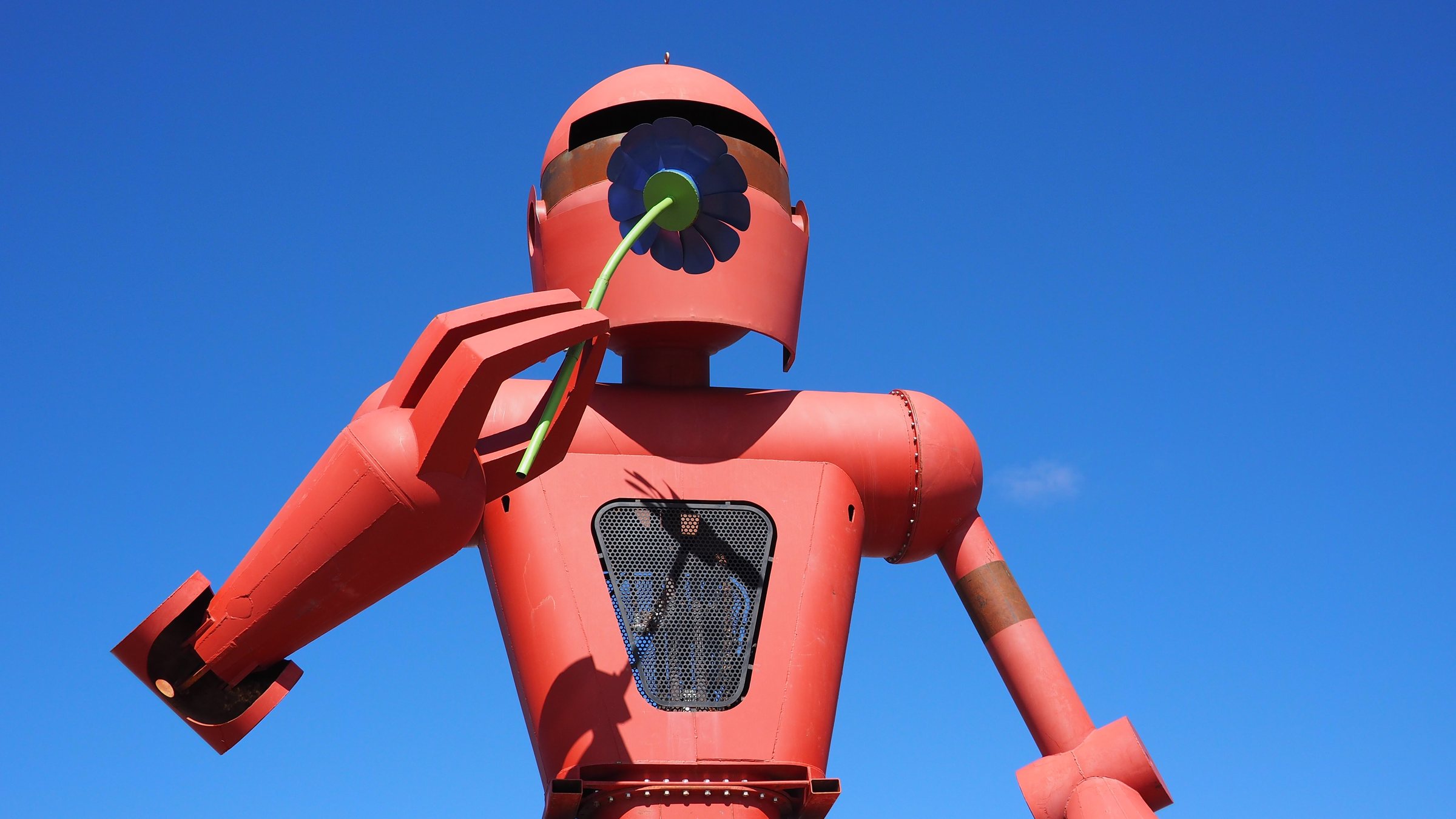 The head and torso of a giant red robot sculpture with a round helmet against a blue sky