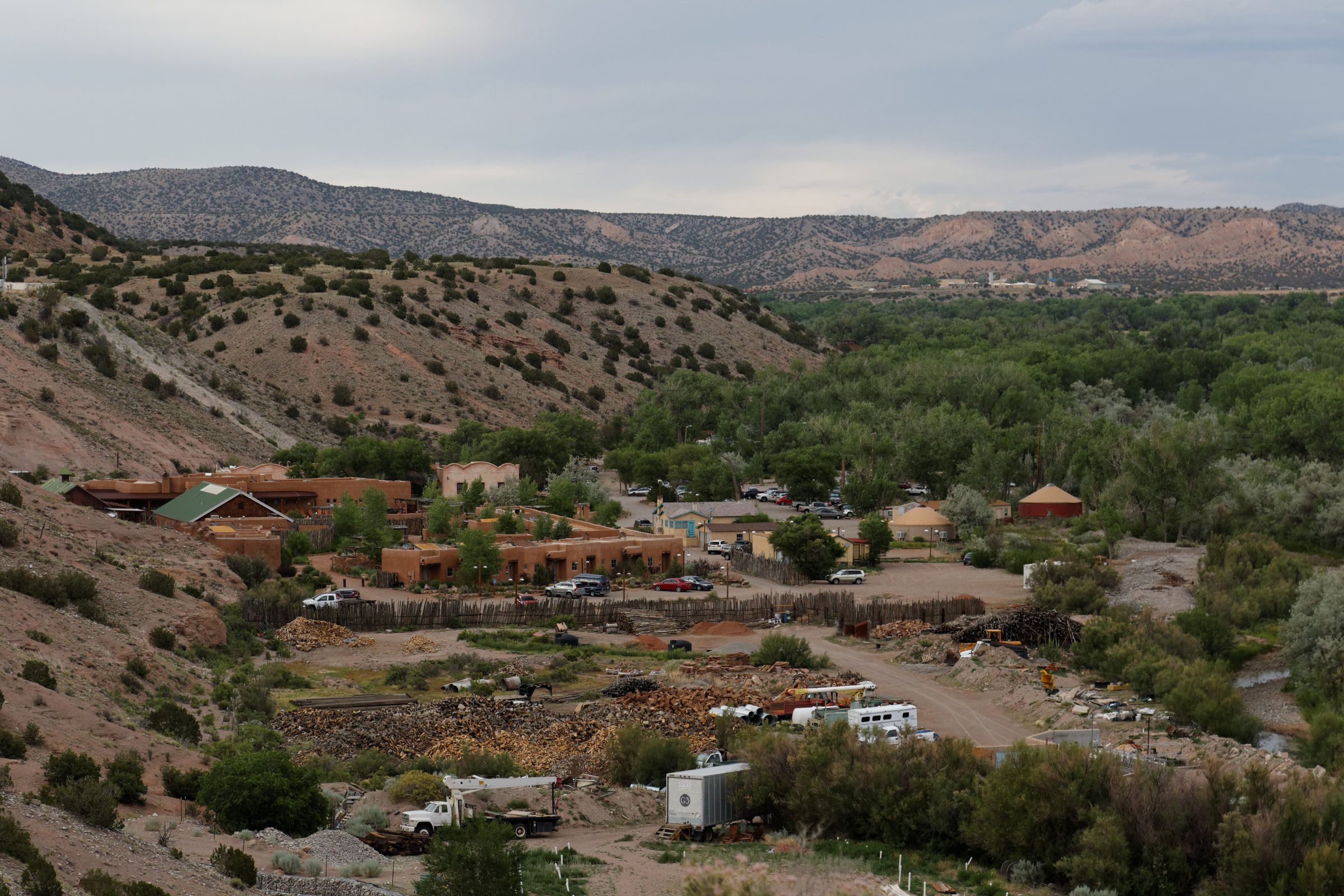 A green river valley with cottonwoods and resort buildings below tan desert hills and mesas at Ojo Caliente