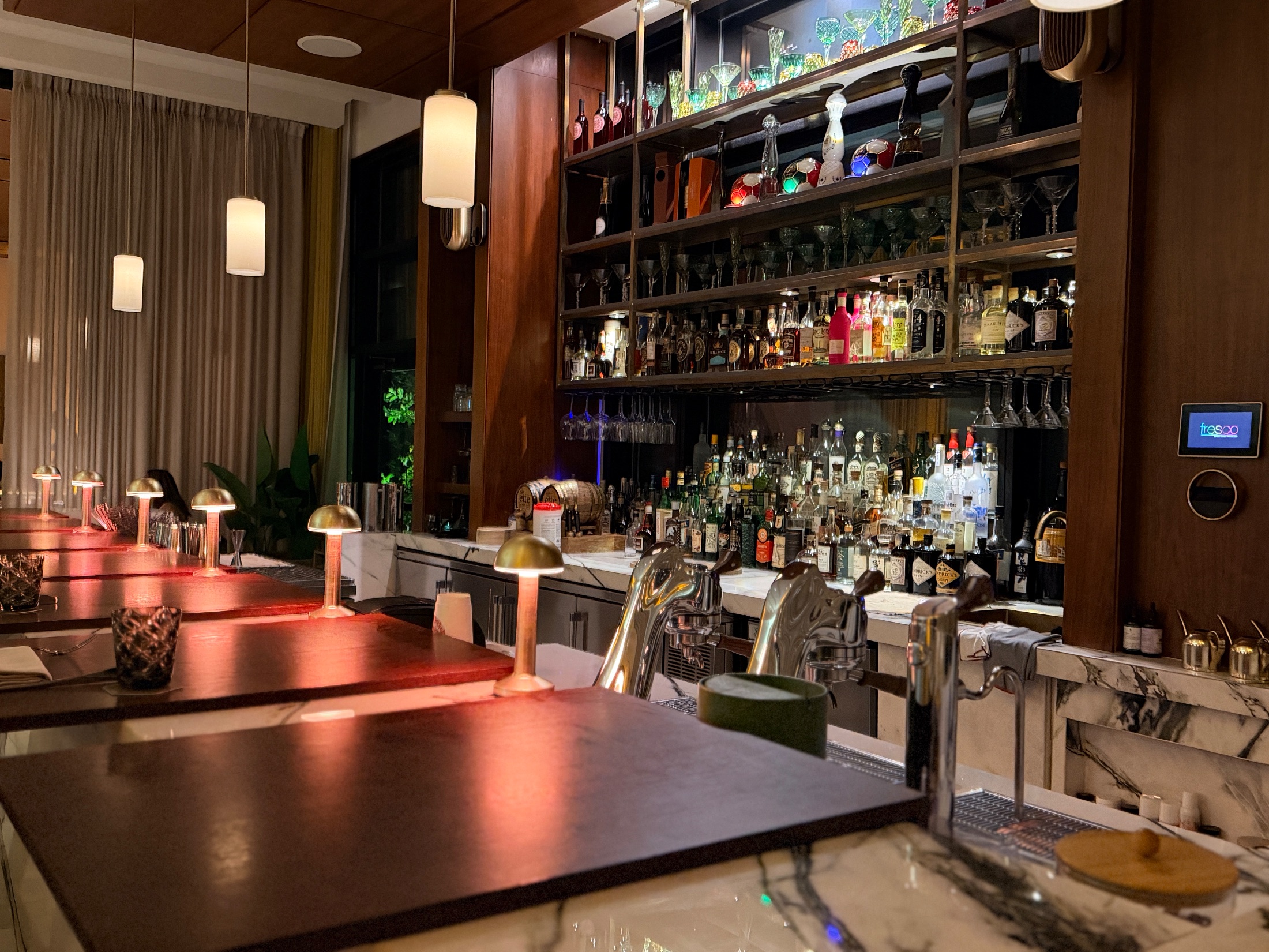 The marble bar at Salt and the Cellar with floor-to-ceiling bottle displays and small brass table lamps