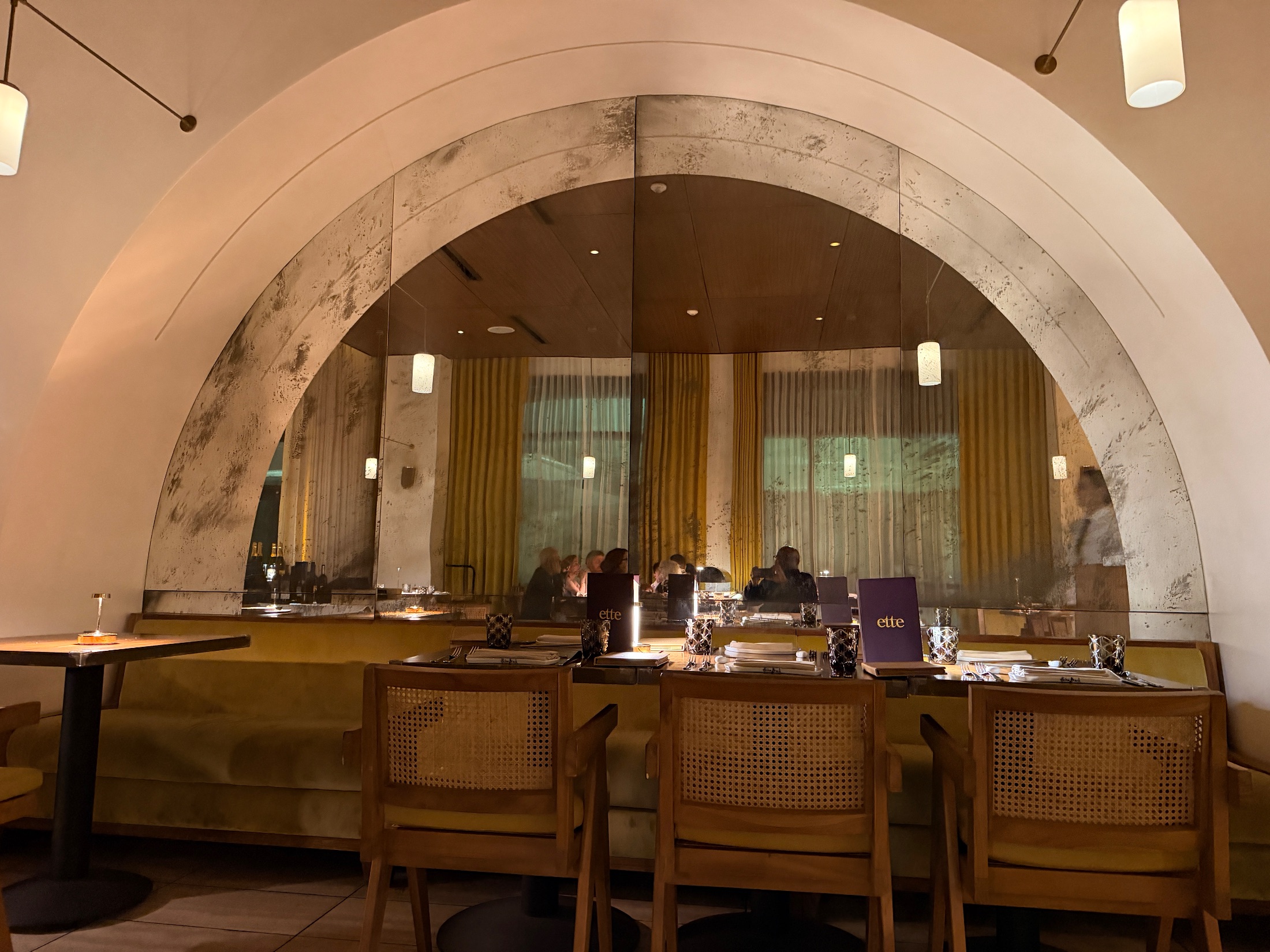The dining room at Salt and the Cellar with an arched antiqued mirror, mustard velvet banquettes, and ette menus on the tables