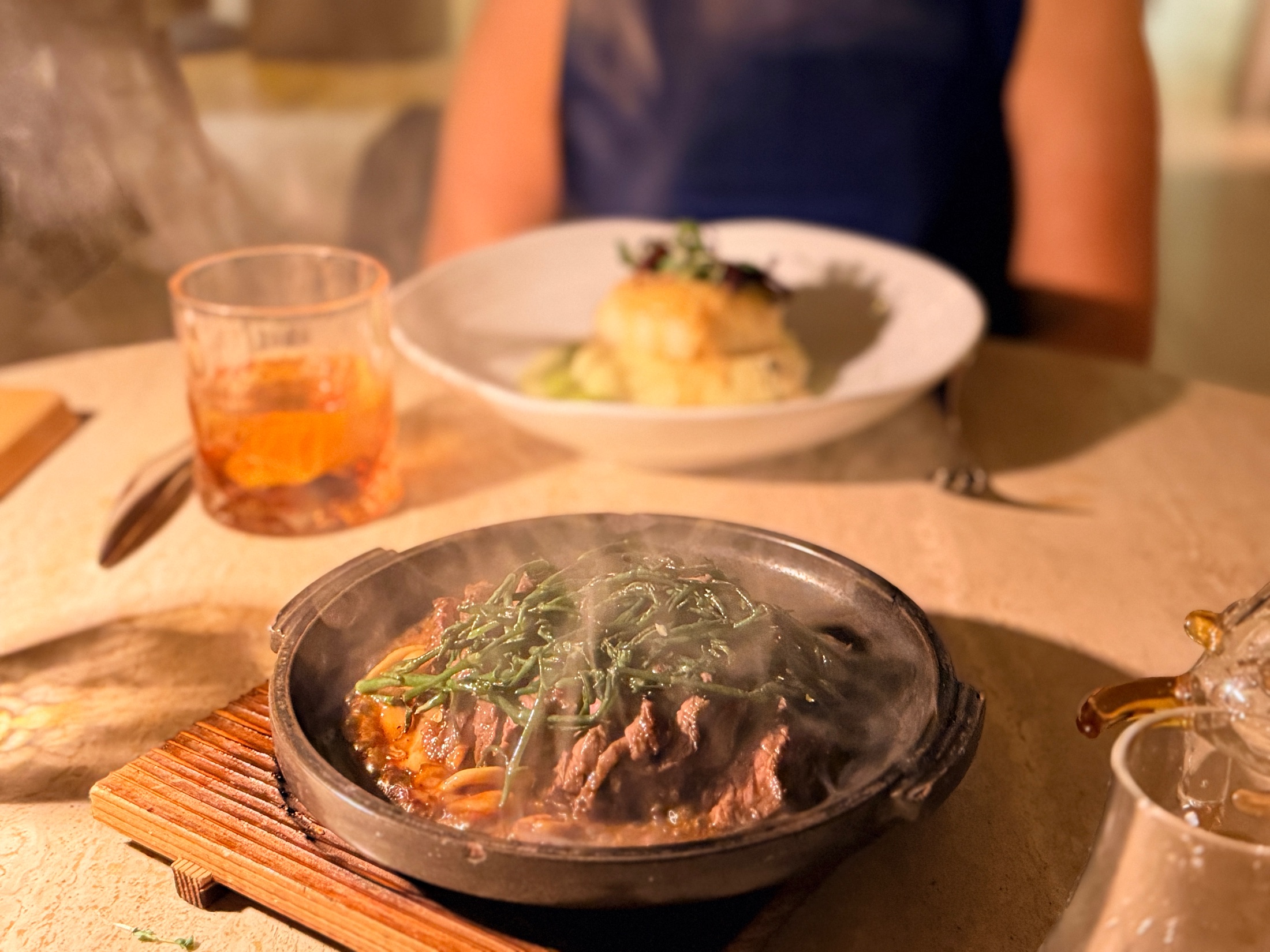 A steaming cast iron pot of braised beef with greens on a wooden trivet at Salt and the Cellar