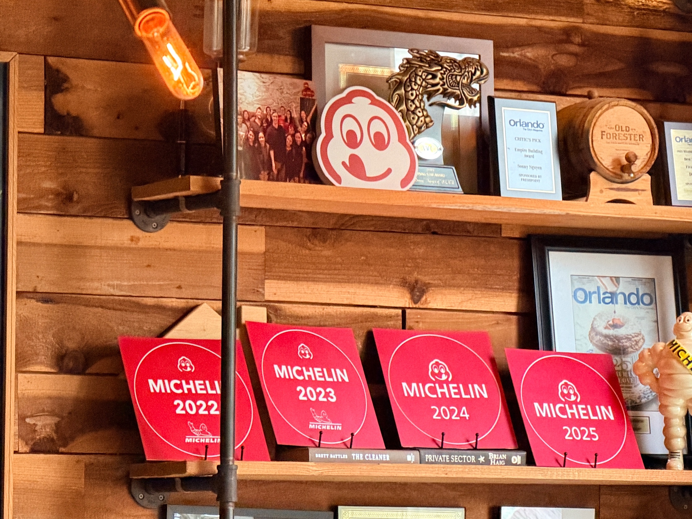 Four Michelin Bib Gourmand plaques for 2022, 2023, 2024, and 2025 displayed on a wood shelf inside DOMU alongside awards and a Michelin figurine